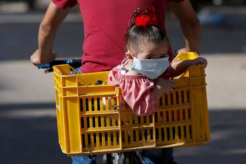 A Palestinian girl wearing a protective face mask looks on as she sits in a box on the back of a bicycle amid the coronavirus disease (COVID-19) crisis, in Gaza City September 27, 2020. REUTERS/Mohammed Salem TPX IMAGES OF THE DAY